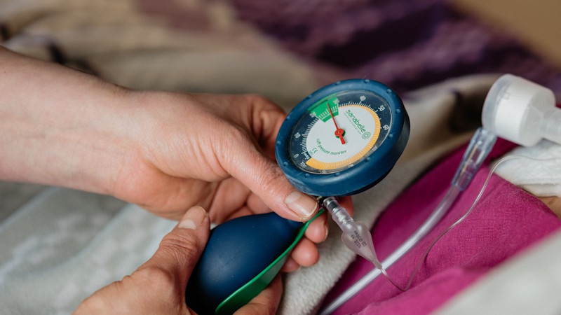 Pflegekraft misst mit einem manuellen Blutdruckmessgerät den Blutdruck einer pflegebedürftigen Person im Rahmen der intensivpflegerischen Versorgung.